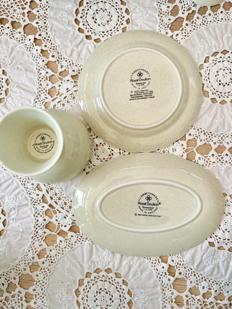 Three pieces of white ceramicware with 'Royal Doulton' branding on a lace tablecloth.