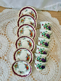 Set of ceramic teacups and saucers with floral and fruit patterns on a lace tablecloth.