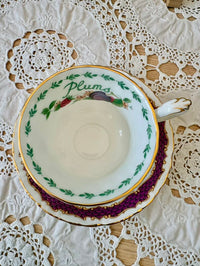 Teacup and saucer with 'Plums' text on a lace tablecloth