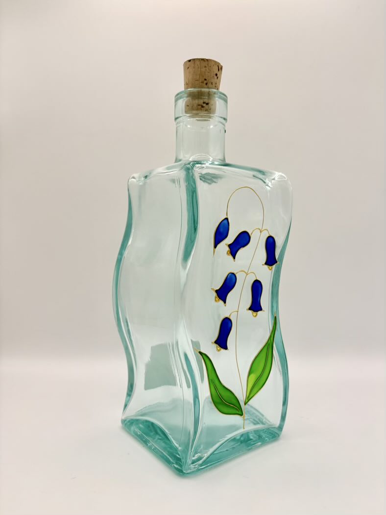 Decorative glass bottle with painted blue flowers and a cork on a white background