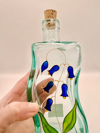 Decorative glass bottle with blue floral design held by a hand against a plain background