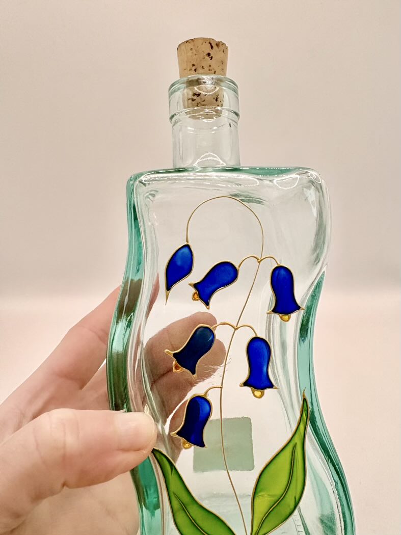 Decorative glass bottle with blue floral design held by a hand against a plain background