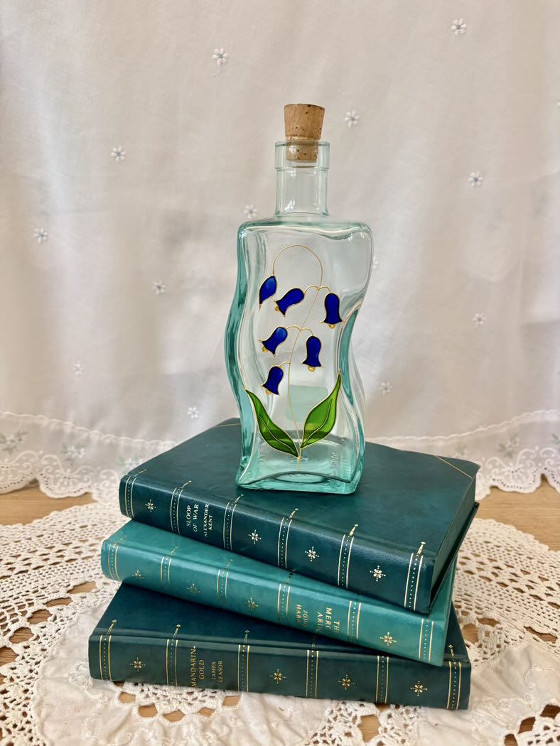 Decorative glass bottle with floral design on a stack of blue books with a lace tablecloth background
