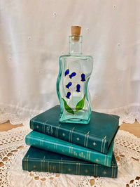 Decorative glass bottle with floral design on a stack of blue books with a lace tablecloth background