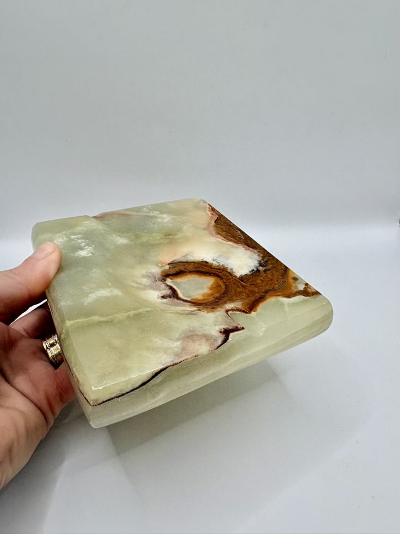 Hand holding a green and brown marbled stone box on a white background