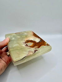 Hand holding a green and brown marbled stone box on a white background