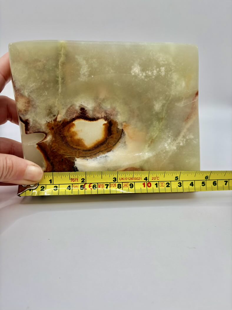 Measuring a green stone with a yellow measuring tape on a white background