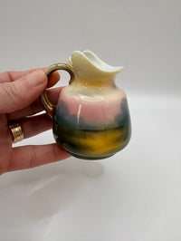 Hand holding a small ceramic pitcher with a gradient color design on a plain background