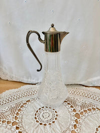 Clear glass carafe with silver metal lid on a lace tablecloth