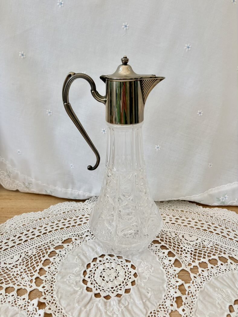 Clear glass carafe with silver metal lid on a lace tablecloth