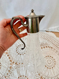 Hand holding a silver jug over a lace tablecloth