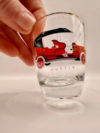 Clear glass with a red car illustration and 'Austin' branding, held by a hand.