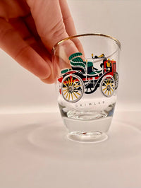 Glass with vintage vehicle design and 'Daimler' branding, held by a hand on a light background