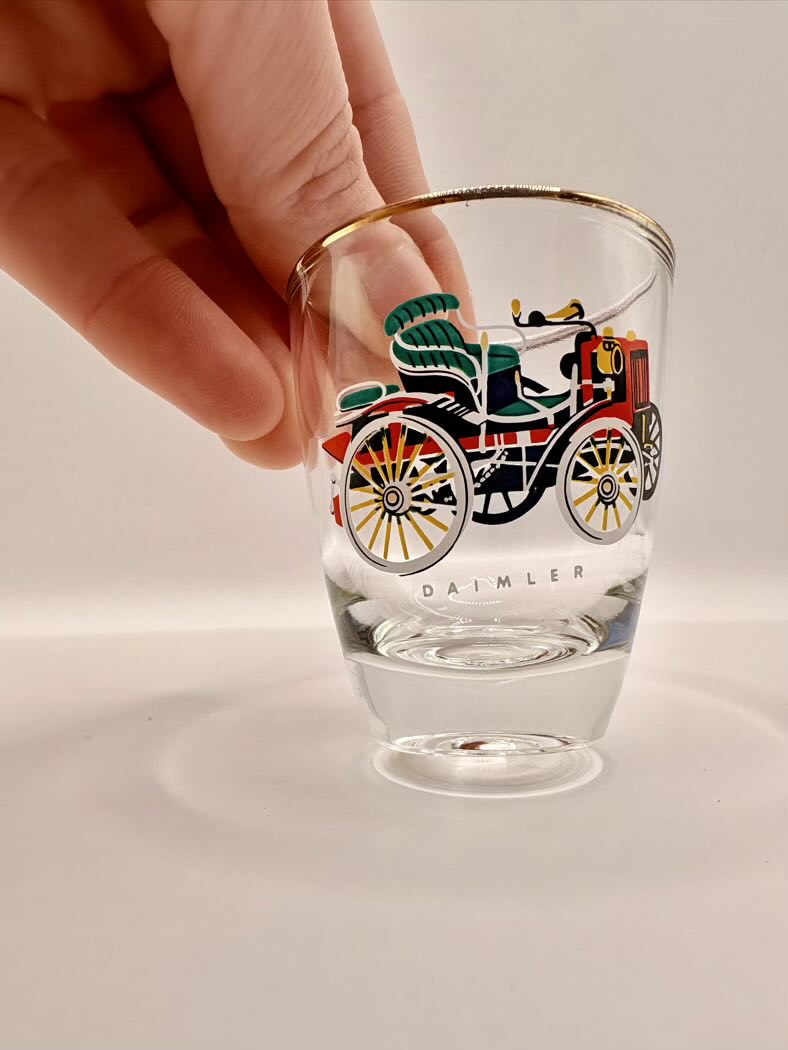 Glass with vintage vehicle design and 'Daimler' branding, held by a hand on a light background
