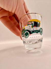 Clear glass with vintage car design held by a hand on a light background