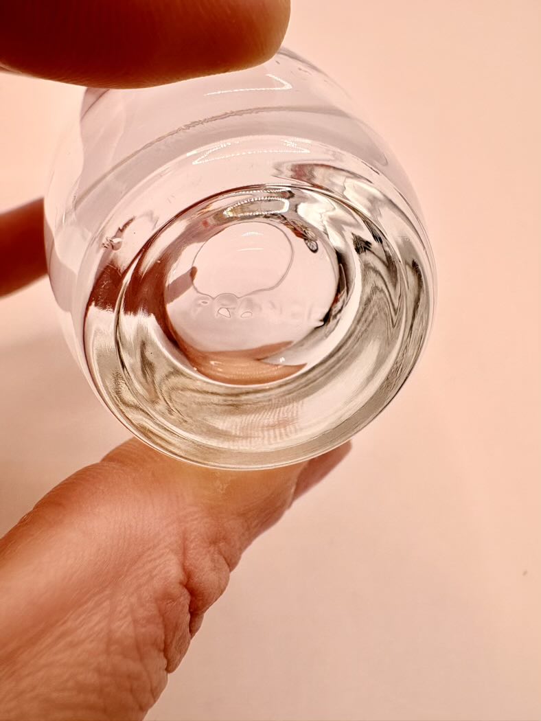 Clear glass bottle held by a hand against a peach-colored background