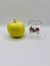 Green apple next to a small glass with a decorative design on a white background