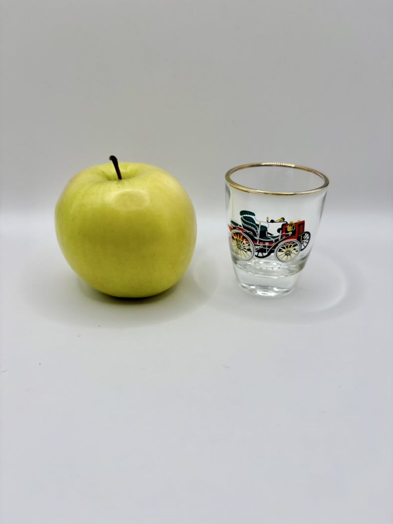 Green apple next to a small glass with a decorative design on a white background
