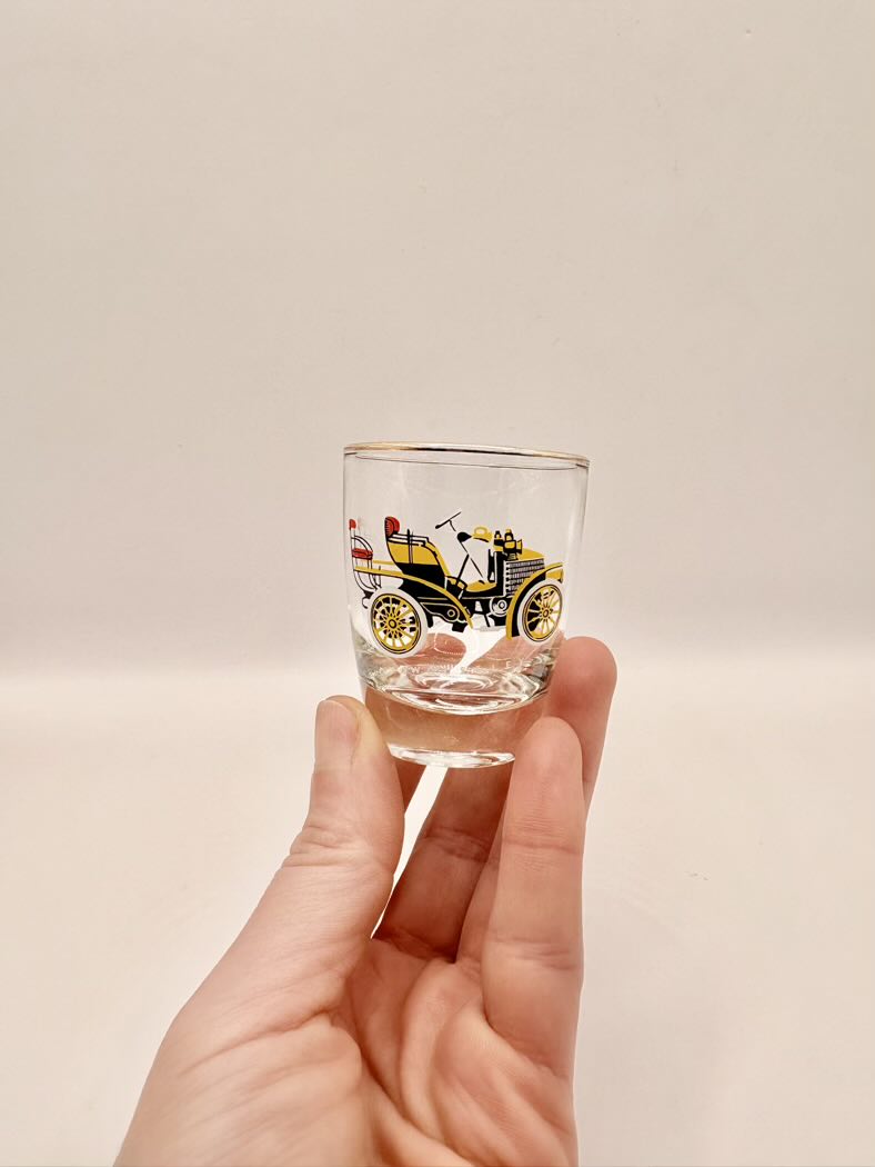 Hand holding a shot glass with vintage car design on a plain background