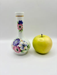 Decorative bottle with floral design next to a yellow apple on a white background
