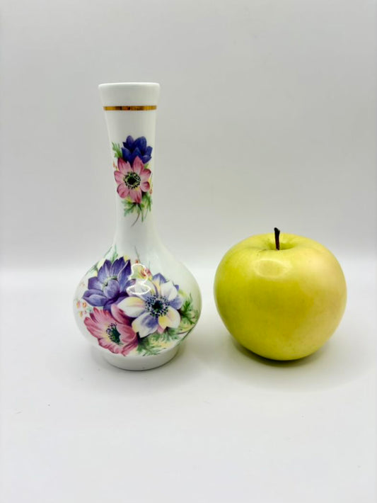 Decorative bottle with floral design next to a yellow apple on a white background