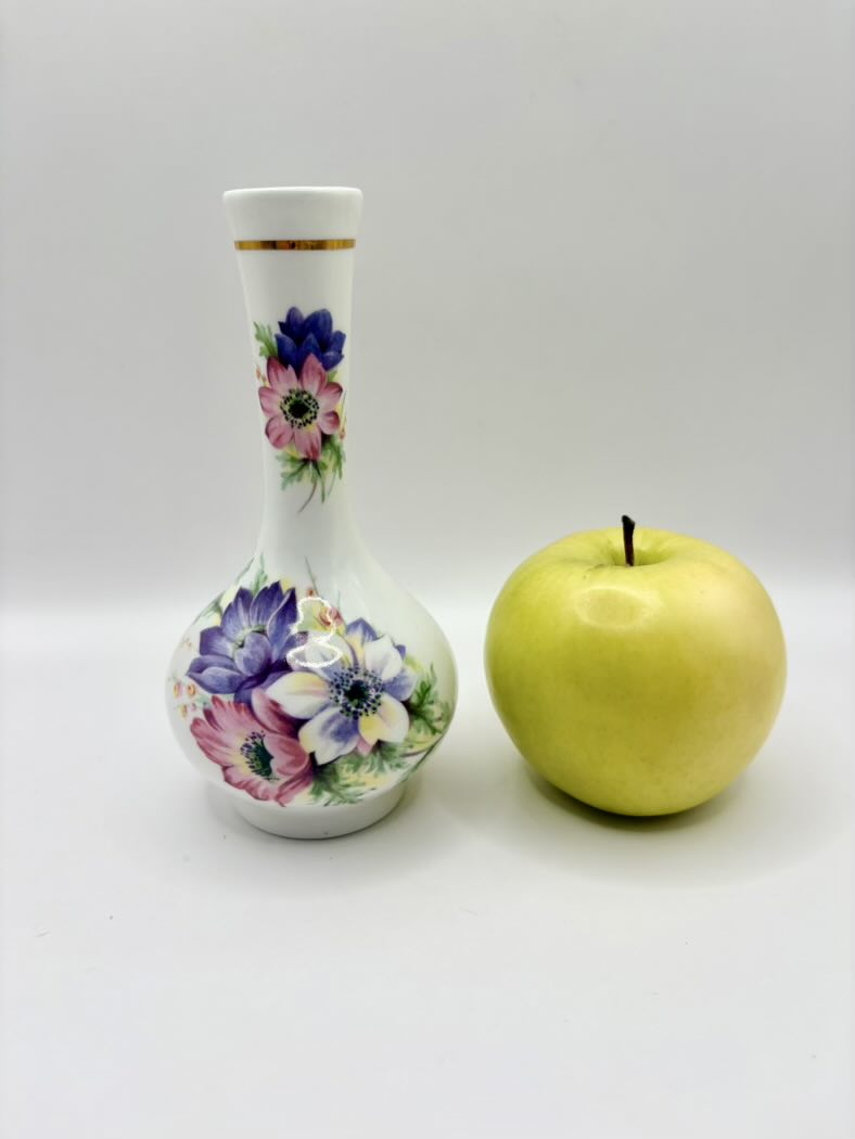 Decorative bottle with floral design next to a yellow apple on a white background