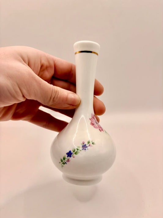 Hand holding a small white vase with floral designs on a plain background