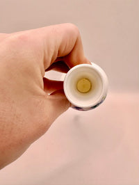 Hand holding a small white container with a yellow object inside against a beige background