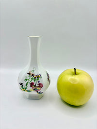 Decorative vase with floral patterns next to a green apple on a white background