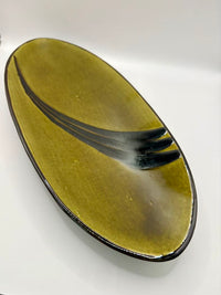 Oval ceramic plate with a greenish-brown glaze and black accent on a white background