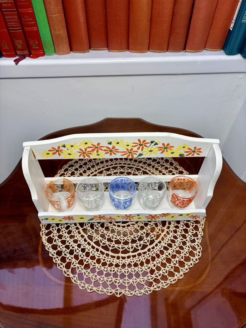 Decorative tray with floral design holding small cups on a wooden surface.