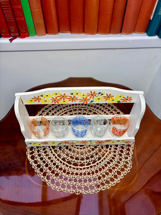 Decorative tray with floral design holding small cups on a wooden surface.