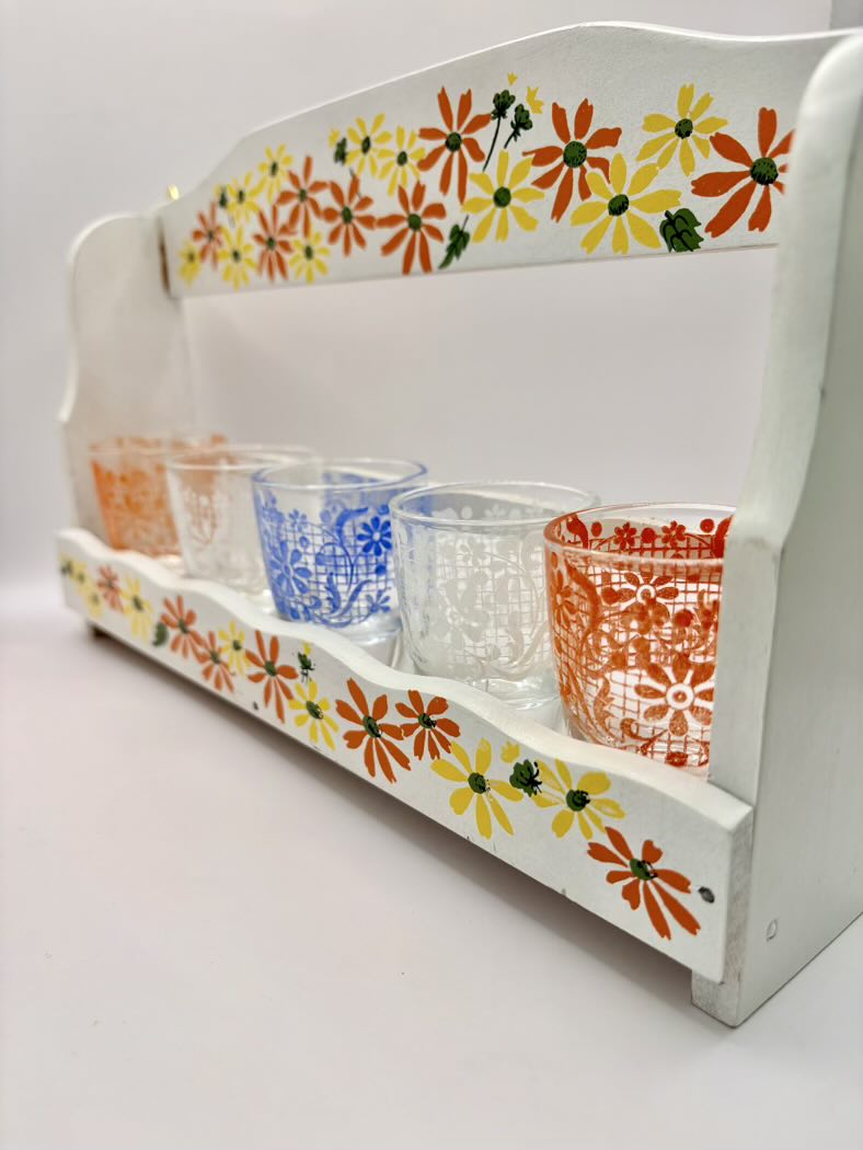 White shelf with floral designs holding colorful glass cups on a white background