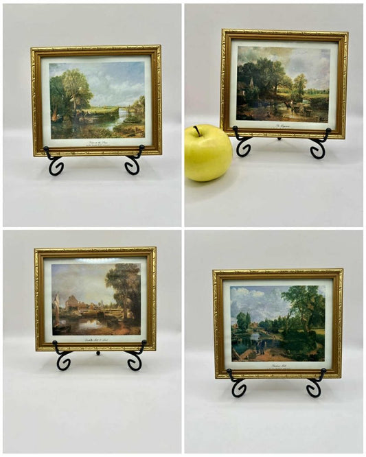 Four gold-framed paintings on stands with a yellow apple in the center.