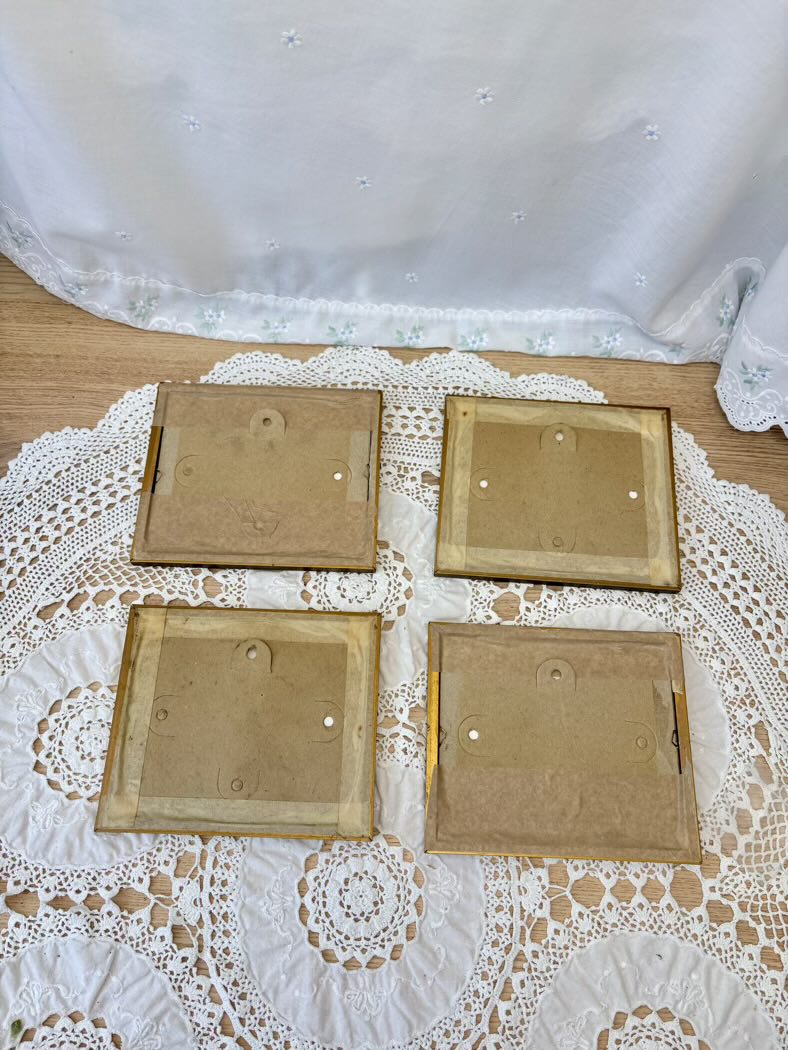 Four back paintings on a lace tablecloth with a white curtain in the background
