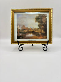 Framed painting of a landscape with a river and buildings on a white background
