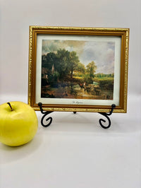 Framed landscape painting on a stand with a yellow apple next to it