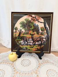 Framed cross-stitched landscape with cows on a white doily