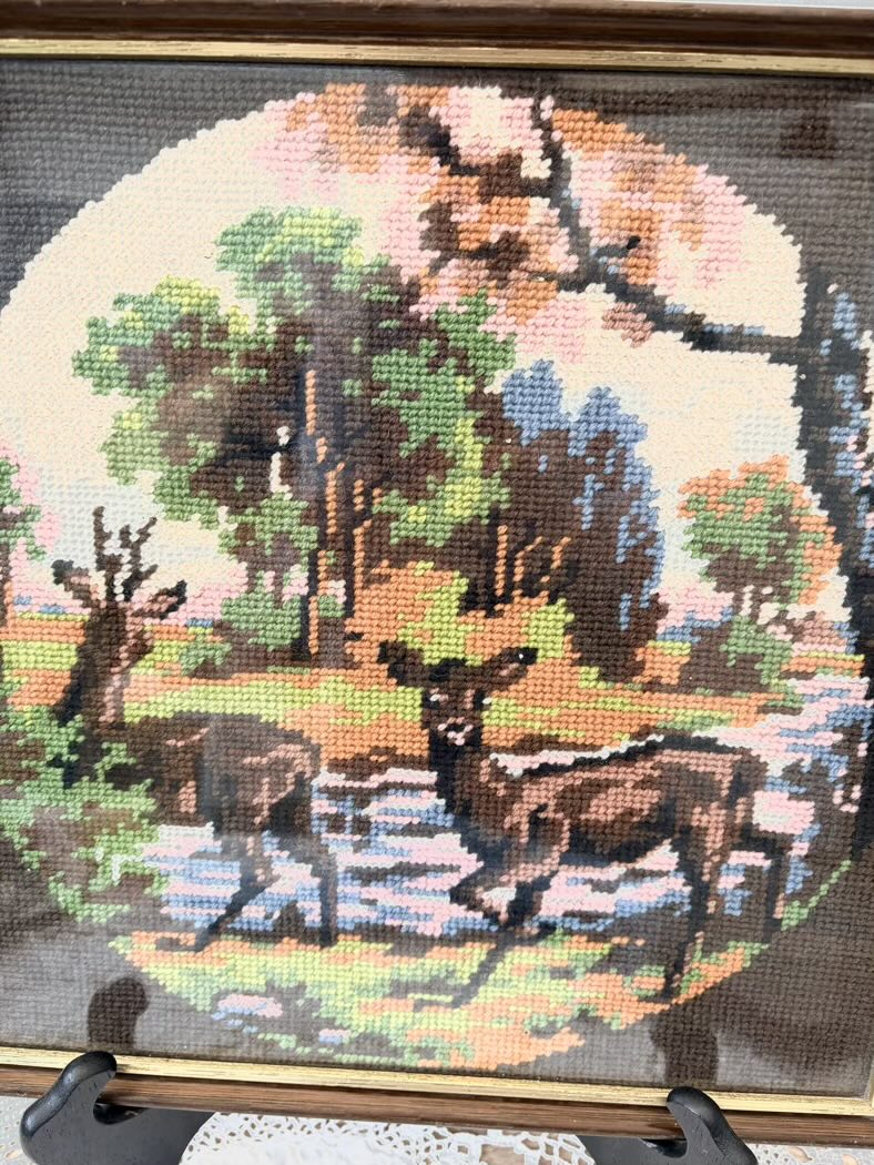Cross-stitched scene of deer in a forest with trees and grass.