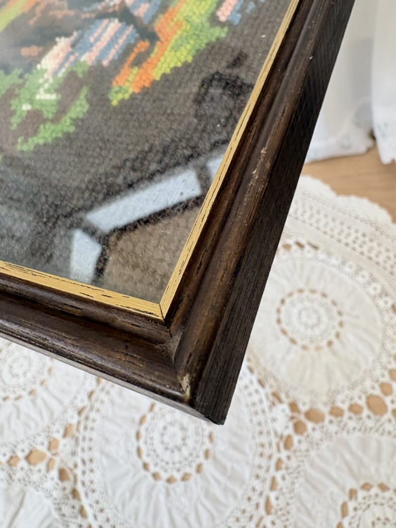 Close-up of a framed cross-stitched piece on a lace tablecloth