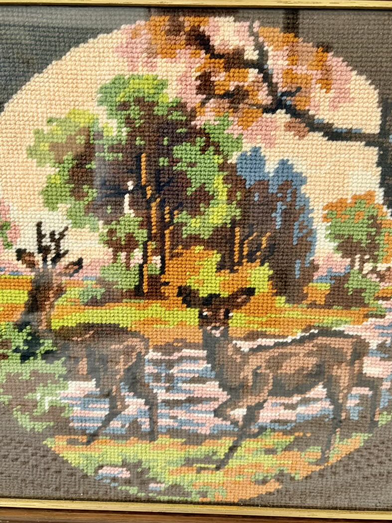 Cross-stitched scene of deer in a forest with trees and grass.