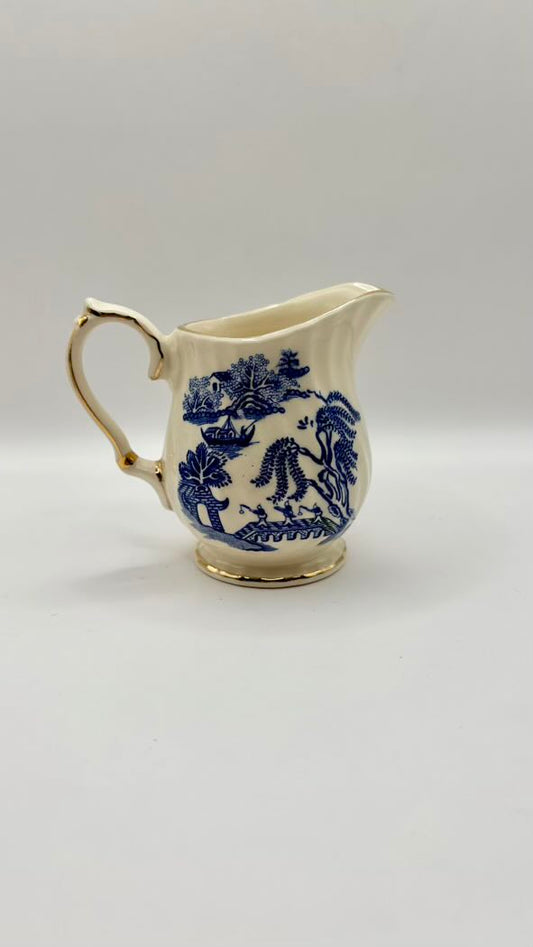 White ceramic creamer with blue floral patterns on a light gray background