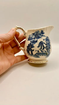 Hand holding a small white ceramic pitcher with blue floral patterns on a plain background