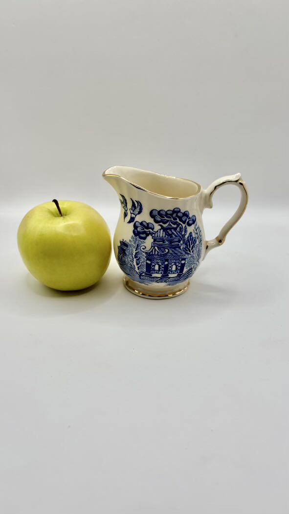 Ceramic pitcher with blue floral design next to a green apple on a white background