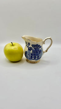 Ceramic pitcher with blue floral design next to a green apple on a white background
