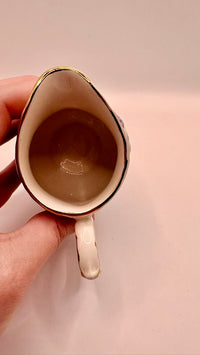 Person holding a small pitcher with a beige interior against a plain background