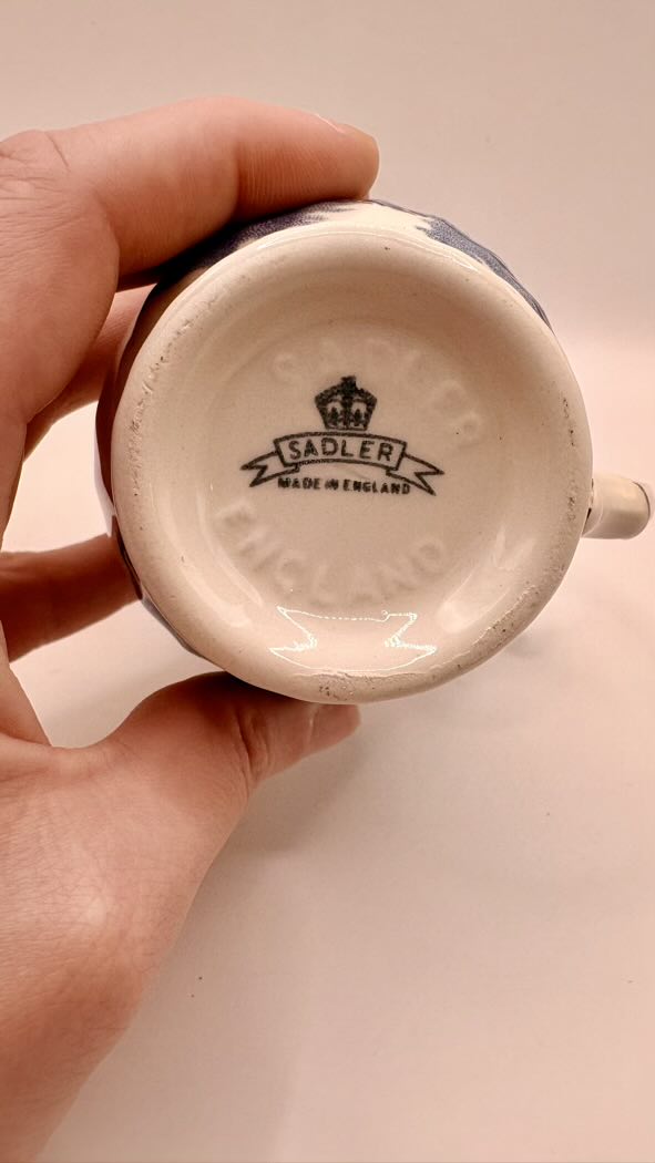 Hand holding a ceramic mug with 'Sadler Made in England' branding on a plain background