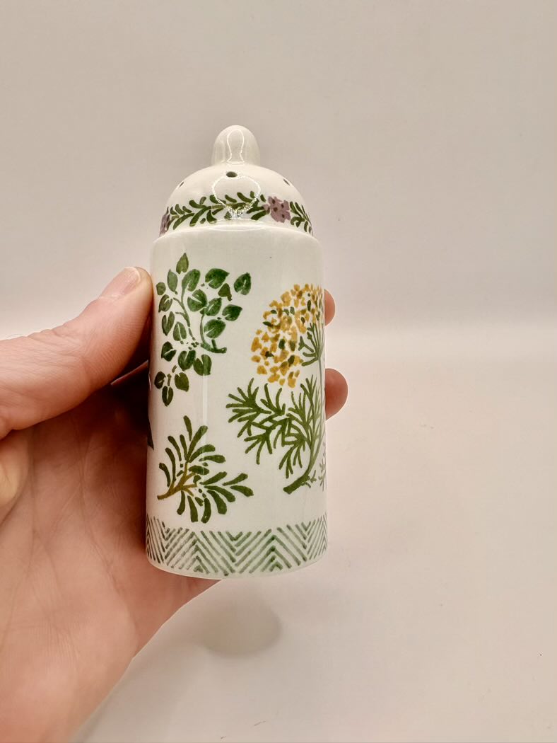 Hand holding a ceramic container with floral designs on a plain background