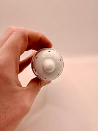 Hand holding a white ceramic object against a beige background