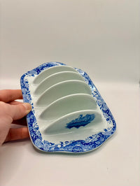 Blue and white ceramic butter dish with a hand holding it on a white background